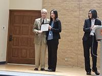 People on a stage holding a certificate and smiling for the camera. 